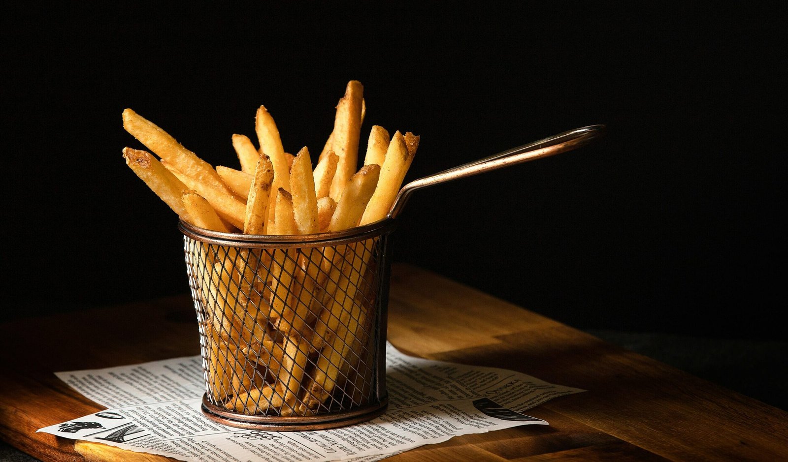 zdjęcie frytek w koszyczku stojącym na stole wyłożonym gazetą