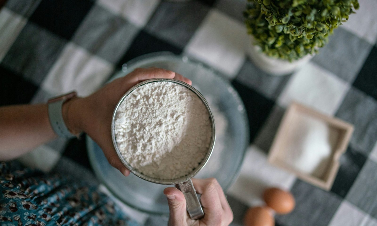 zdjęcie rąk przesiewających mąkę ziemniaczaną bez glutenu przez sitko do miski na stole