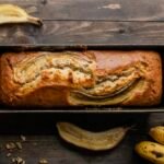 bezglutenowy chlebek bananowy w keksówce na stole w towarzystwie bananów i orzechów włoskich