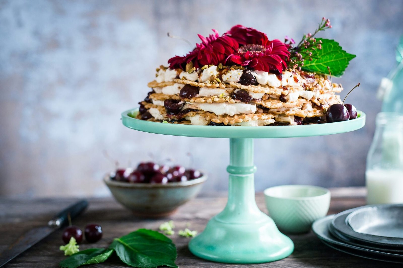 Bezglutenowy tort z kremem, wiśniami i kwiatami, elegancko podany na miętowej paterze