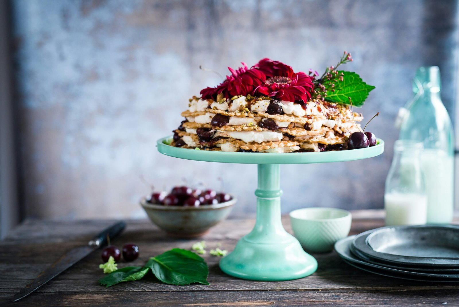 Bezglutenowy tort z kremem, wiśniami i kwiatami, elegancko podany na miętowej paterze