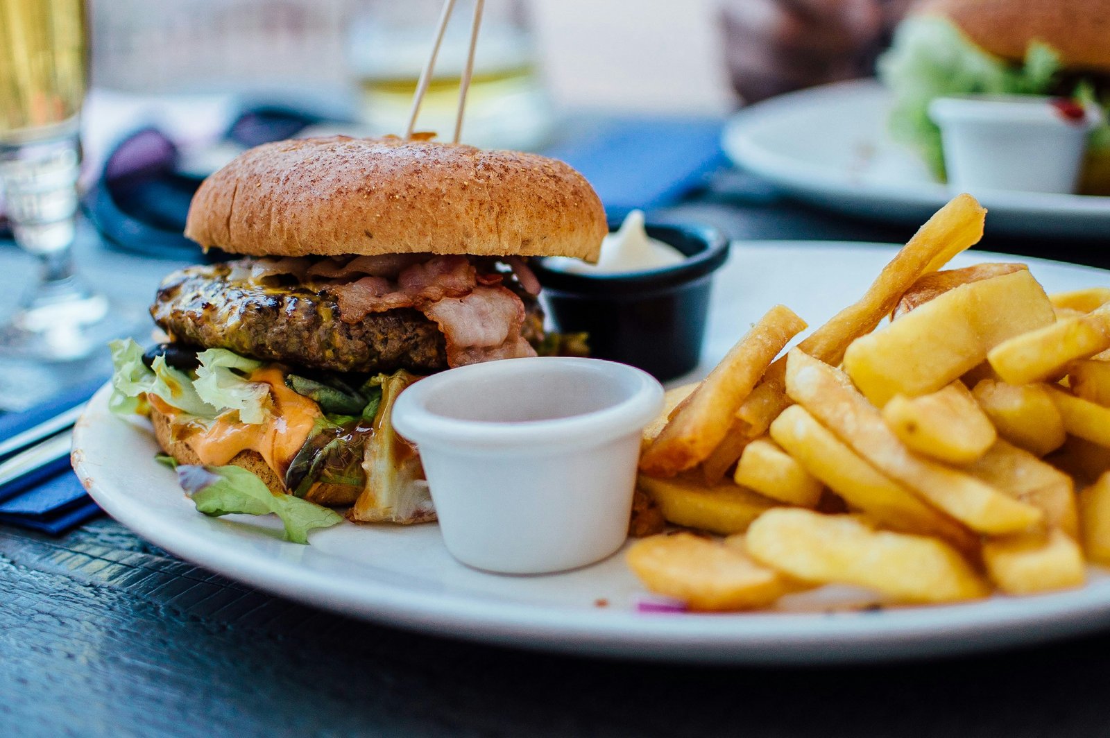 Bezglutenowy burger z soczystym mięsem, boczkiem, sałatą i frytkami, serwowany z sosem