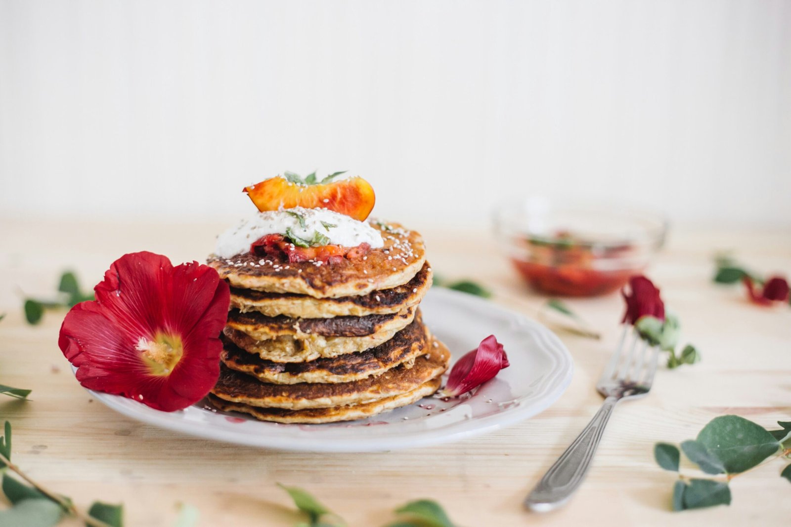 zdjęcie bezglutenowych pancakes ułożonych w stosik na talerzu udekorowanym kwiatami i liśćmi