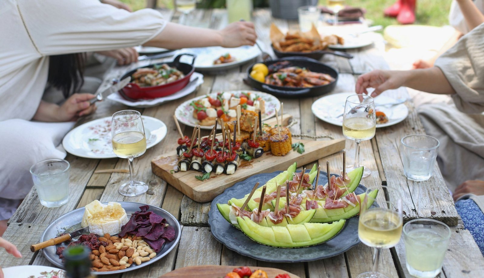 stołu w ogrodzie zastawionego bezglutenowymi przekąskami i napojami po które sięga kilka osób