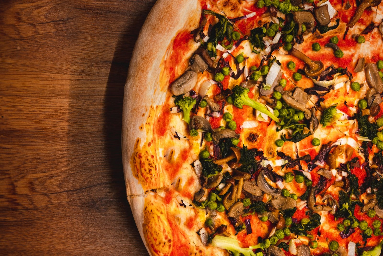 zdjęcie fragmentu pizzy z warzywami i sosem pomidorowym bez glutenu położonej na drewnianym stole