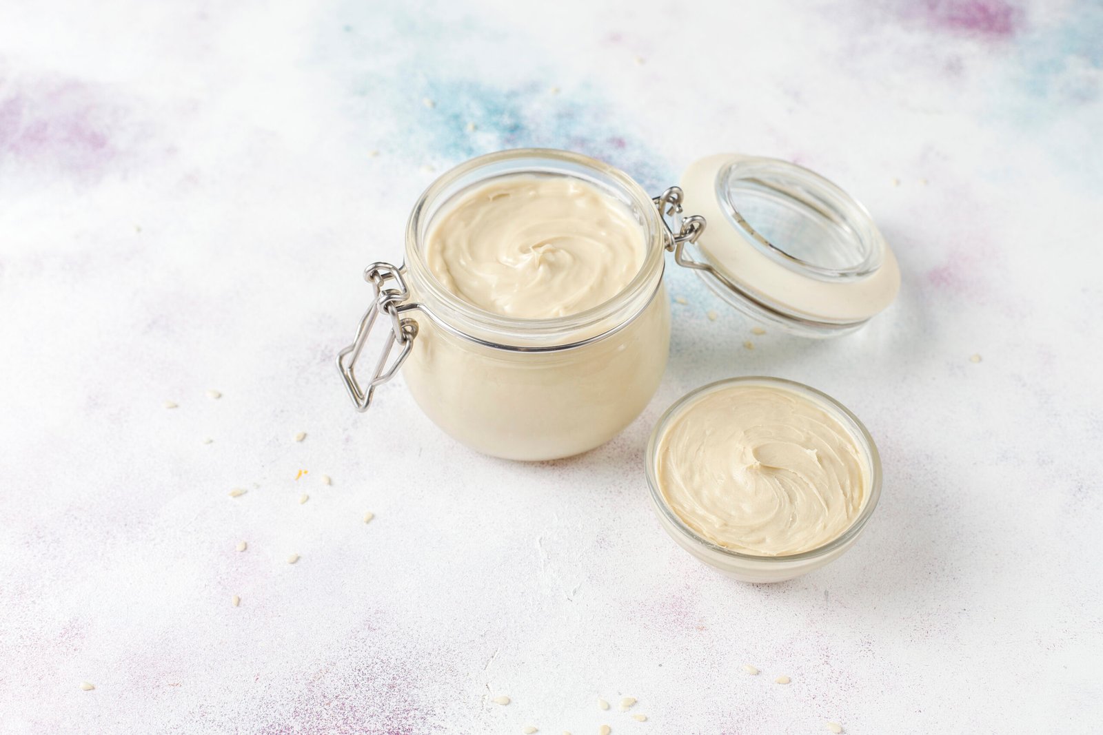 zdjęcie domowego majonezu bez glutenu w przezroczystym słoiczku z zamykaniem oraz w miseczce, na kolorowym tle