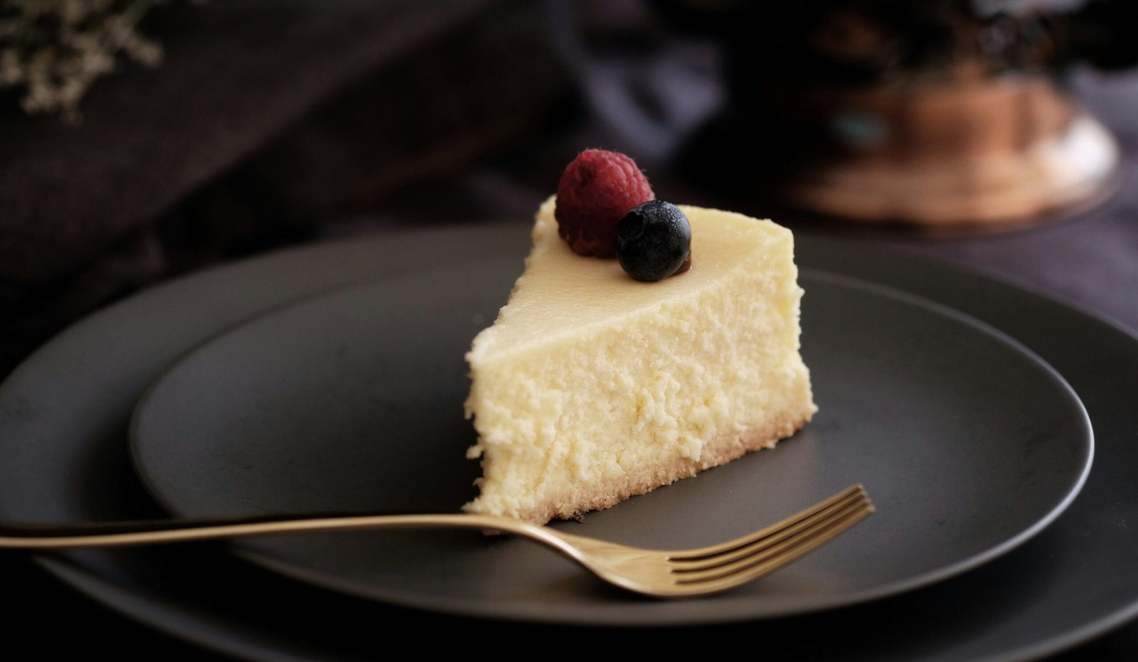 zdjęcie kawałka sernika bezglutenowego na kruchym spodzie, podanego na czarnym talerzu z owocami na wierzchu