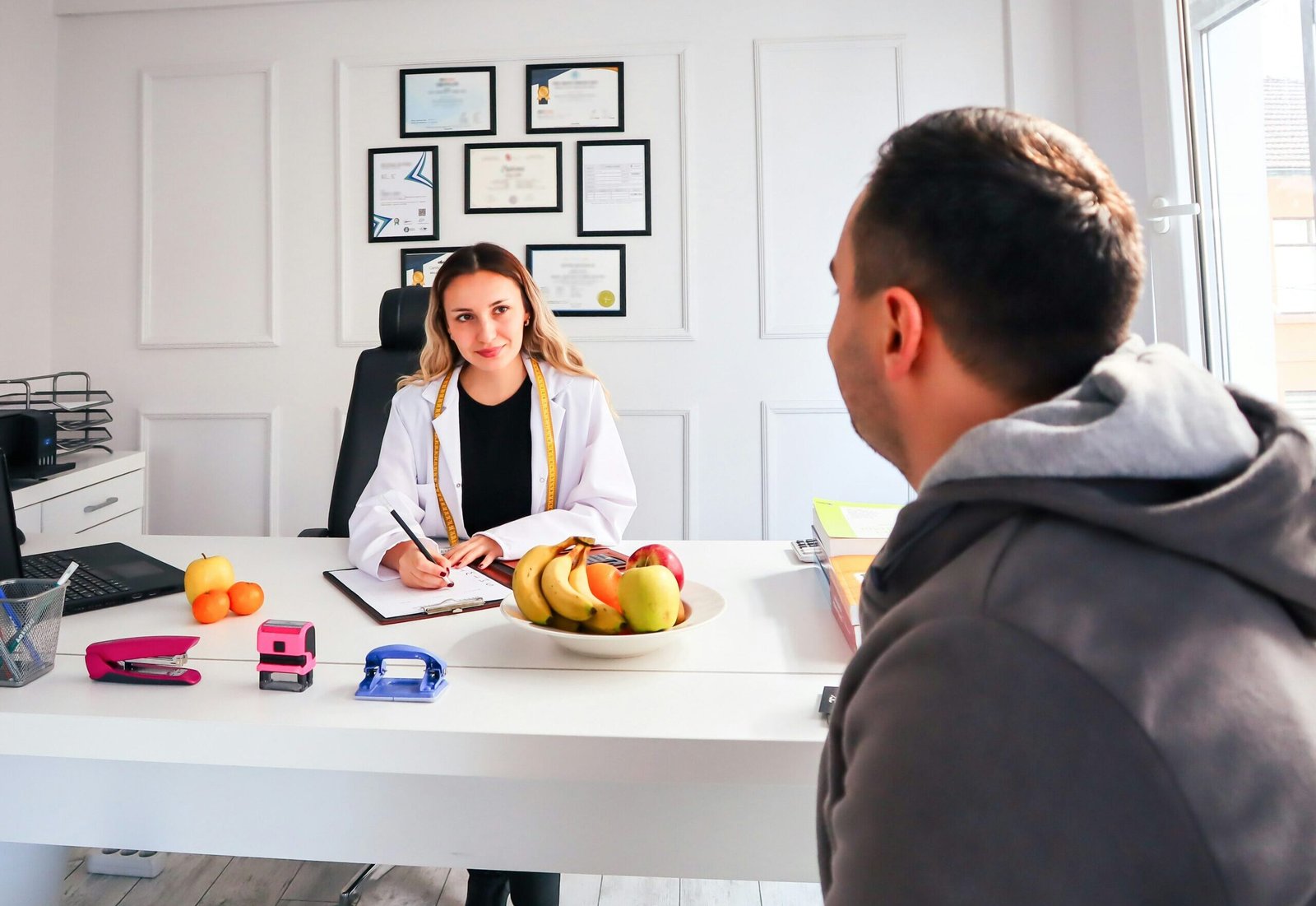 Konsultacja dietetyczna – dietetyk rozmawia z pacjentem w gabinecie, na biurku owoce jako symbol zdrowej diety