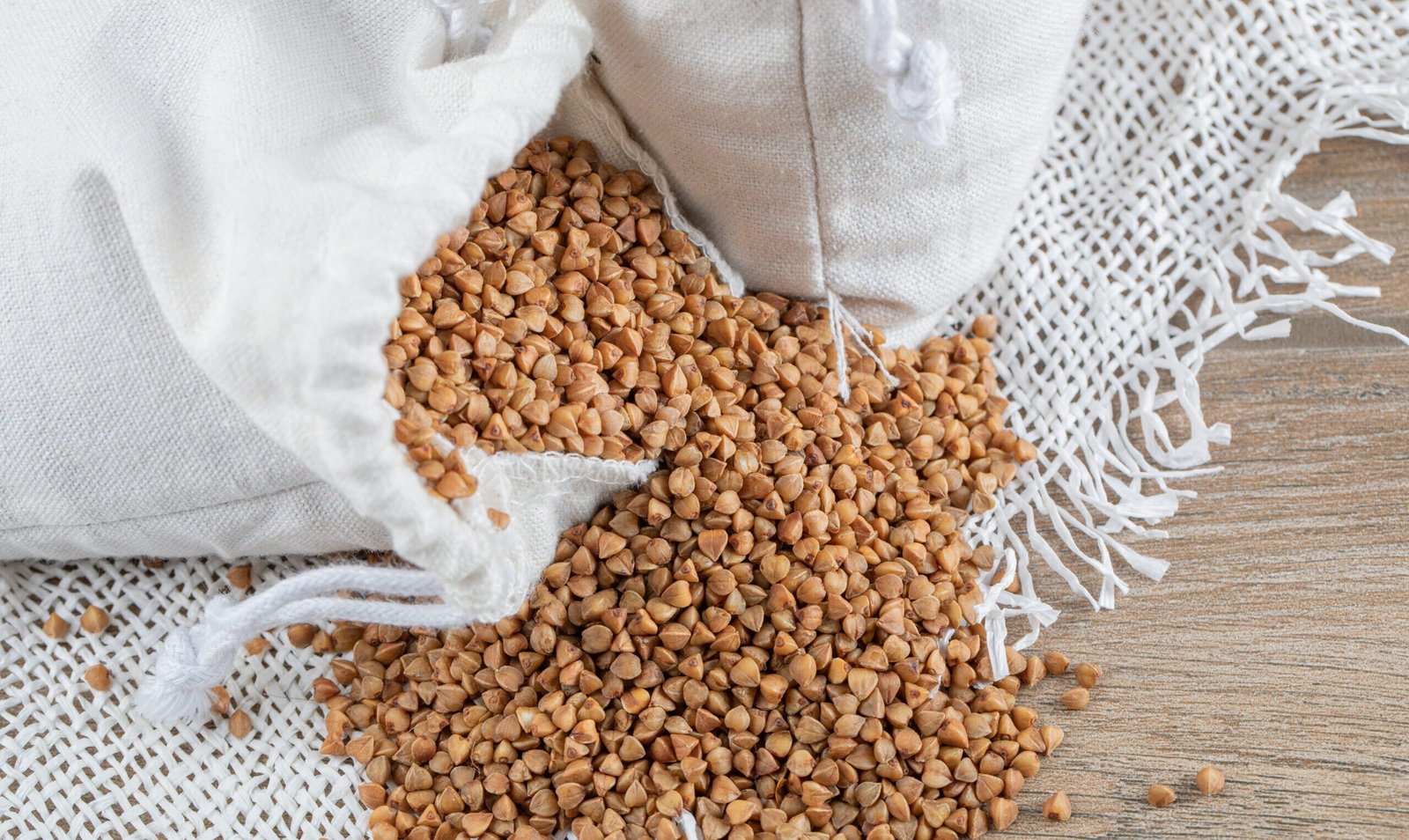 zdjęcie gryki wysypującej się z białego woreczka na drewniany stół przykryty białym obrusem