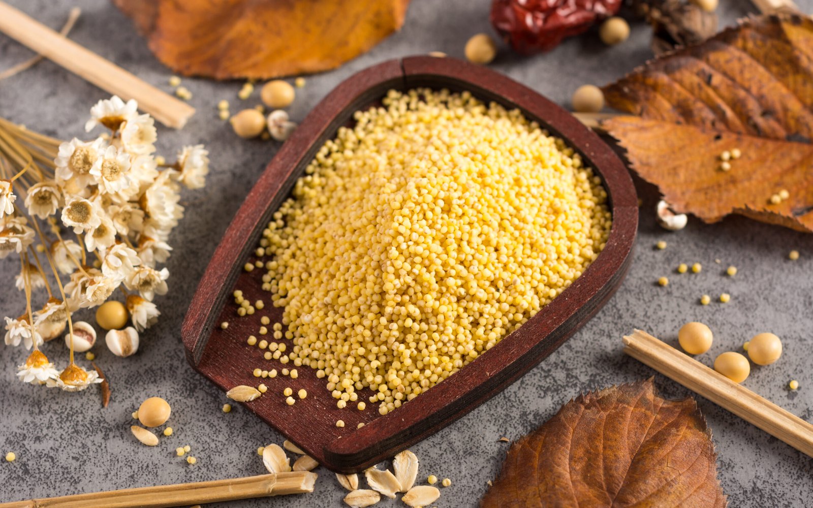 zdjęcie proso w drewnianej miseczce na stole w otoczeniu suszonych kwiatów i liści