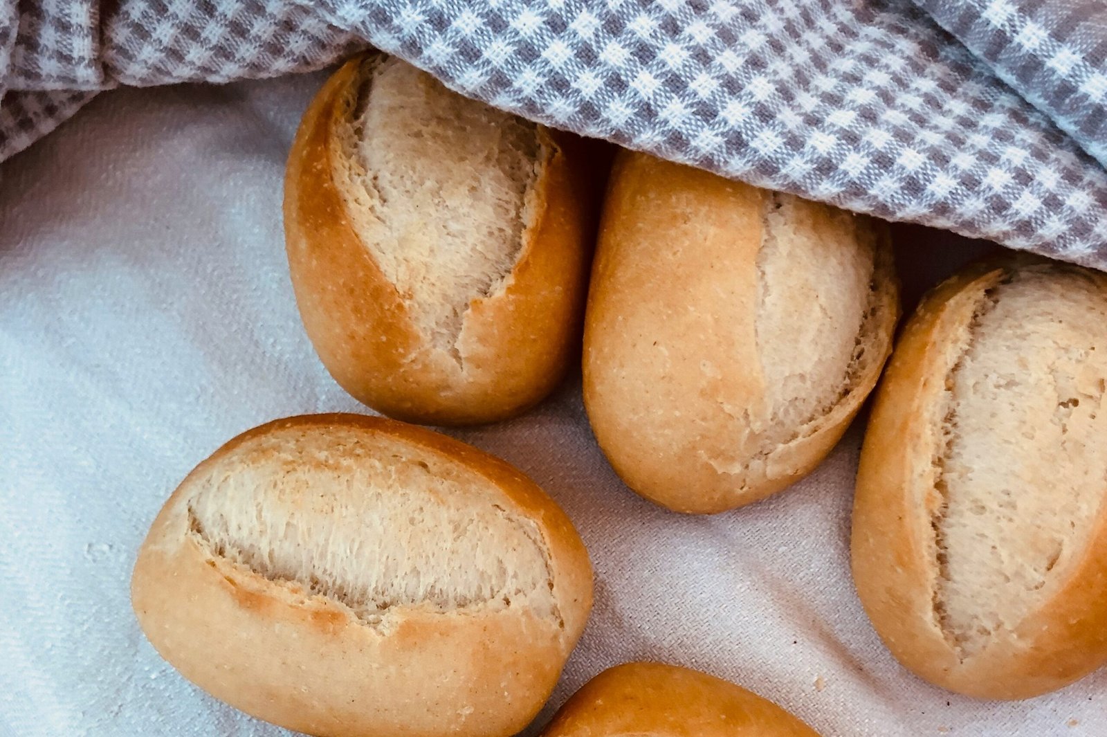 Złociste, chrupiące bułki bezglutenowe przykryte ściereczką, świeżo upieczone i gotowe do podania.