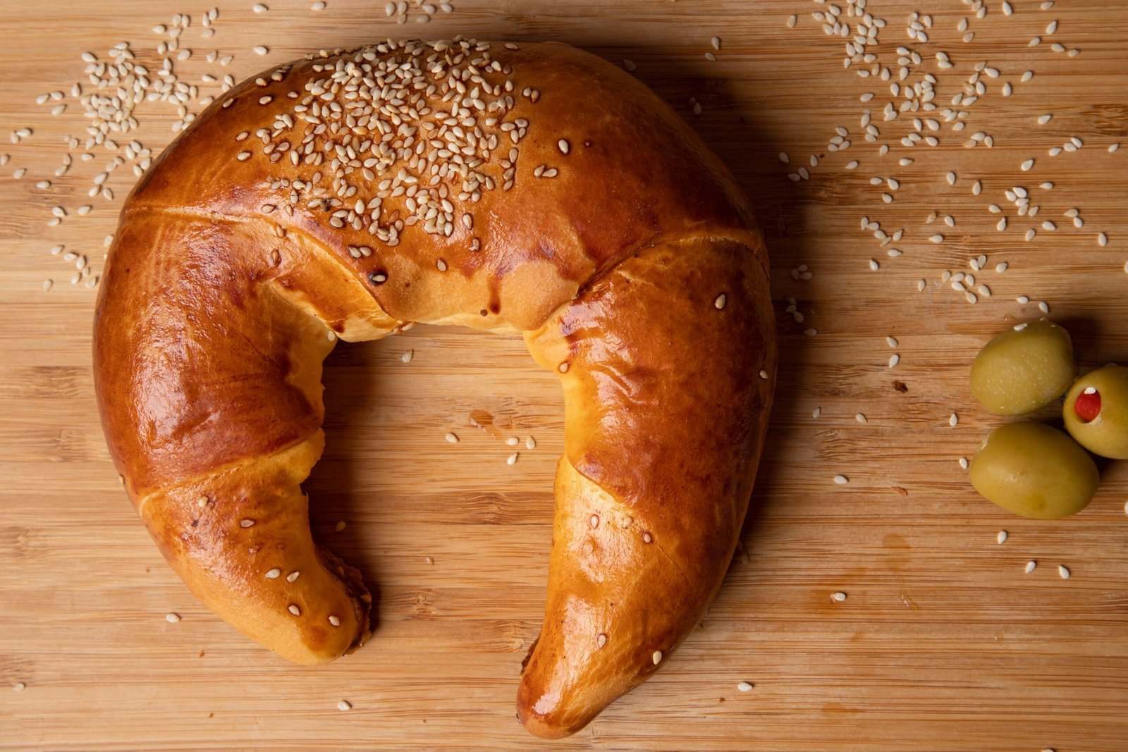 zbliżenie na bezglutenowego rogalika z sezamem na drewnianym stole obok oliwek