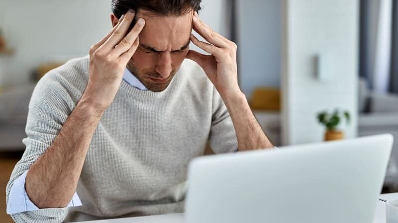 Mężczyzna z bólem głowy przy komputerze – stres jako możliwy czynnik wyzwalający objawy celiakii.