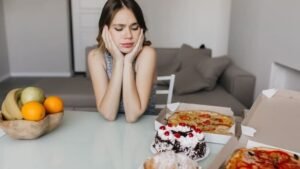 Smutna kobieta patrzy na pizzę i ciasto, unikając glutenu z powodu celiakii – objawy nietolerancji glutenu u dorosłych.
