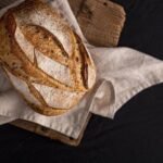 Domowy chleb bezglutenowy o złocistej, chrupiącej skórce i miękkim wnętrzu, ułożony na lnianej ściereczce – pyszne domowe pieczywo bez glutenu.