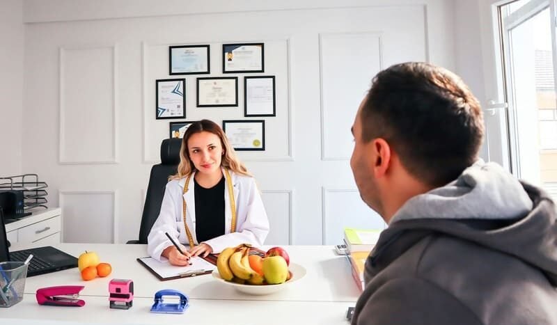 Konsultacja dietetyczna – dietetyk rozmawia z pacjentem w gabinecie, na biurku owoce jako symbol zdrowej diety