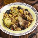 Miska gulaszu z kawałkami mięsa, warzywami i ziarnami, podana na drewnianym stole obok suszonych owoców i tradycyjnych naczyń