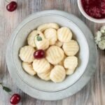 Bezglutenowe kluski leniwe na słodko z twarogu, podane w misce z wiśniami i sosem owocowym – delikatne pierogi leniwe bez glutenu.