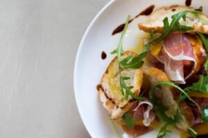 zdjęcie zbliżenia na sałatkę z szynką parmeńską, grzankami bez glutenu polaną sosem balsamicznym na białym talerzu
