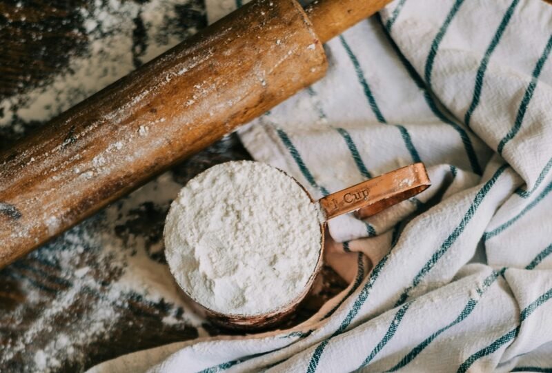 zdjęcie przestawiające stół z wałkiem, mąką i ścierką, zasypany mąką bezglutenową