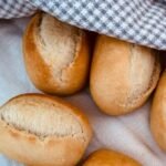 Złociste, chrupiące bułki bezglutenowe przykryte ściereczką, świeżo upieczone i gotowe do podania.