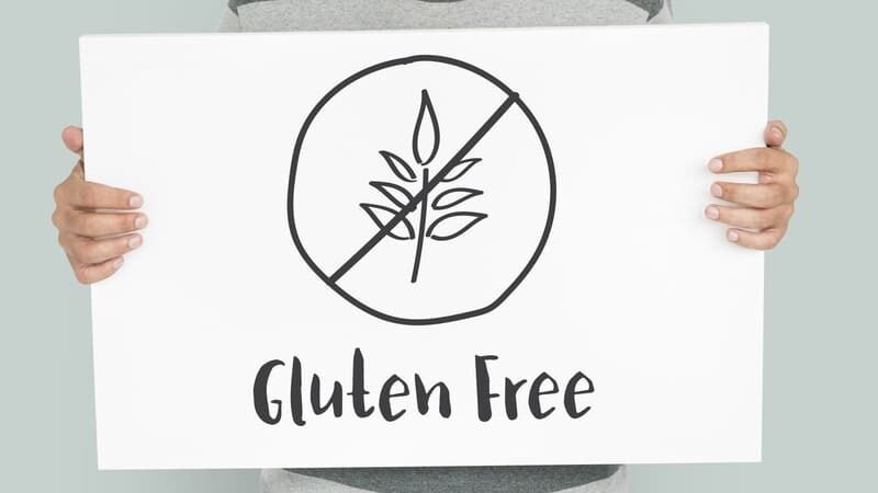 Osoba trzyma tablicę z symbolem przekreślonego kłosa i napisem Gluten Free – oznaczenie diety bezglutenowej