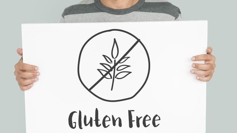 Osoba trzyma tablicę z symbolem przekreślonego kłosa i napisem Gluten Free – oznaczenie diety bezglutenowej