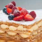 Bezglutenowe ciasto francuskie przekładane kremem budyniowym, posypane cukrem pudrem i udekorowane świeżymi truskawkami, malinami i borówkami.