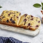 zdjęcie bezglutenowego ciasta z owocami podanego na drewnianej desce w towarzystwie miseczki borówek