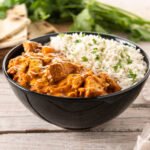 Bezglutenowe curry z kurczakiem w sosie pomidorowym, podane z ryżem jaśminowym i świeżymi ziołami w czarnej misce