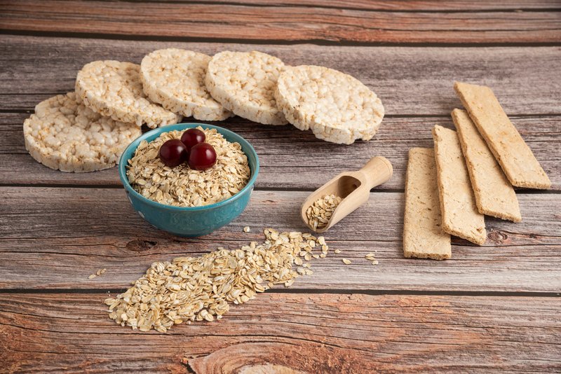 zdjęcie przedstawiające bezglutenowe płatki owsiane, wafle kukurydziane i ryżowe na drewnianym stole