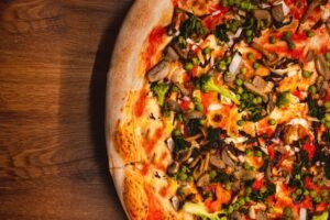 zdjęcie fragmentu pizzy z warzywami i sosem pomidorowym bez glutenu położonej na drewnianym stole
