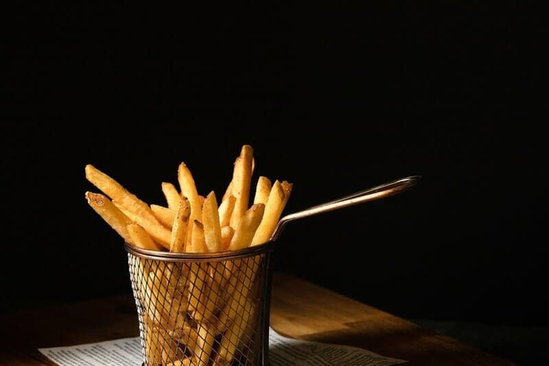 zdjęcie frytek w koszyczku stojącym na stole wyłożonym gazetą