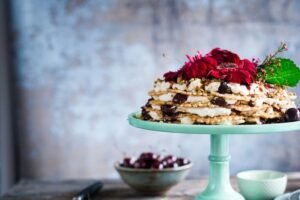 Bezglutenowy tort z kremem, wiśniami i kwiatami, elegancko podany na miętowej paterze