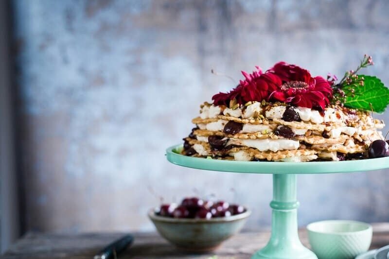 Bezglutenowy tort z kremem, wiśniami i kwiatami, elegancko podany na miętowej paterze