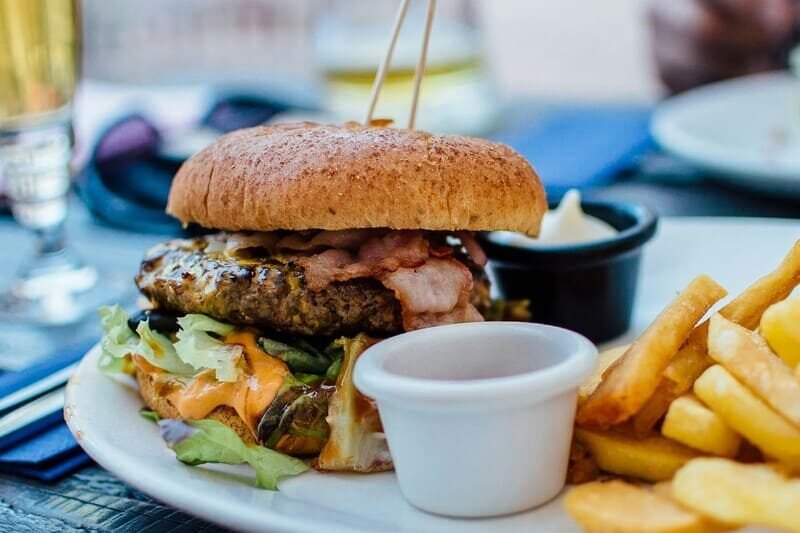 Bezglutenowy burger z soczystym mięsem, boczkiem, sałatą i frytkami, serwowany z sosem