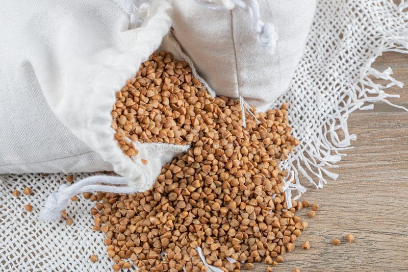 zdjęcie gryki wysypującej się z białego woreczka na drewniany stół przykryty białym obrusem