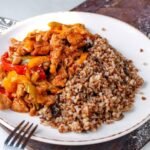 Gulasz wołowy z warzywami podany z kaszą gryczaną bez glutenu na białym talerzu.