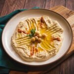 naturalnie bezglutenowy hummus podany na białym talerzu z dodatkiem ziaren ciecierzycy i przypraw