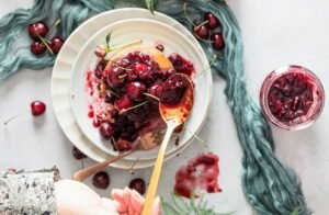 zdjęcie przedstawiające bezglutenowe pancakes z wiśniami i rękę kobiety, która dokłada więcej konfitury
