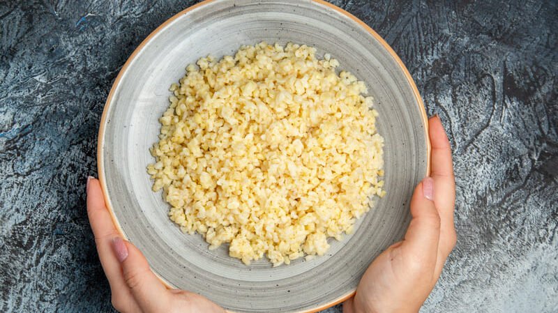 Kasza bulgur w misce trzymanej w dłoniach – pszenna kasza zawierająca gluten, niewskazana na diecie bezglutenowej i przy celiakii