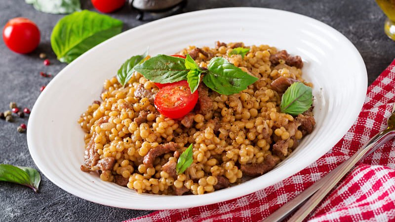 zdjęcie kaszy jęczmiennej bezglutenowej na białym talerzu, przystrojonej listkami bazylii i pomidorkami