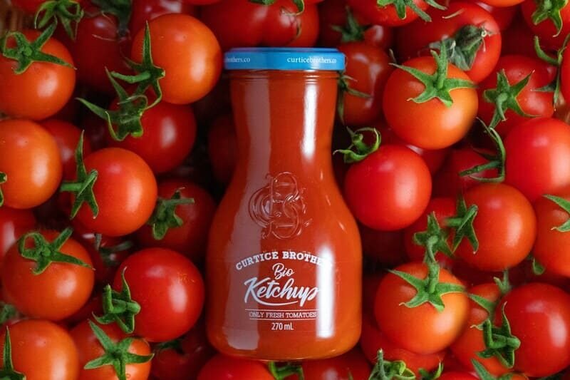 zdjęcie ketchupu w szklanej butelce z etykietą z białymi napisami ułożonego na pomidorach