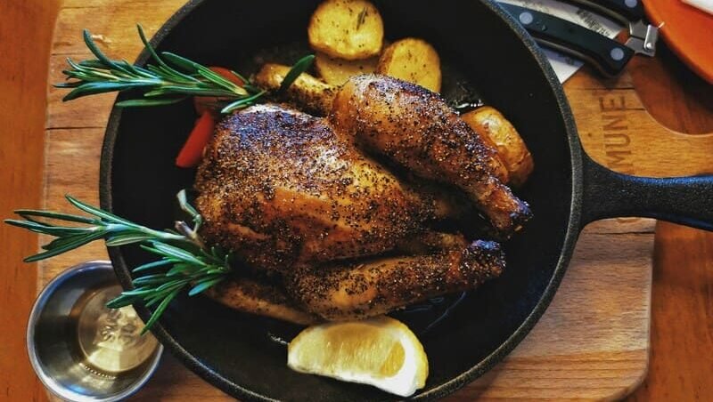 zdjęcie pieczonego kurczaka w całości z cytryną i rozmarynem, całość ustawiona na stole