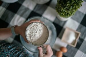zdjęcie rąk przesiewających mąkę ziemniaczaną bez glutenu przez sitko do miski na stole