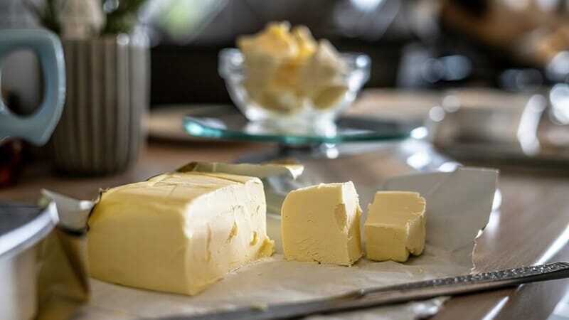 zdjęcie kostki masła pokrojonej nożem, leżącej na opakowaniu z masła