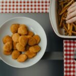 Bezglutenowe nuggetsy z kurczaka podane na białym talerzu, chrupiące kawałki idealne jako sylwestrowa przekąska typu finger food.