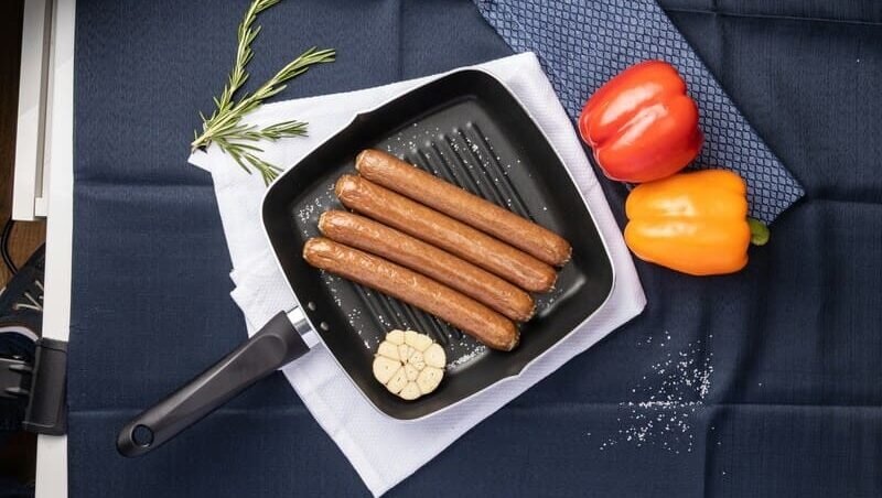 zdjęcie parówek ułożonych obok siebie na patelni grillowej, obok dwie papryki