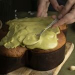 zdjęcie bezglutenowej pasty pistacjowej którą ręka rozsmarowuje na gotowym wypieku drożdżowym na kuchennym stole