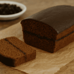 Bezglutenowy piernik świąteczny przecięty w poprzek i przełożony cienką warstwą powideł śliwkowych, ułożony na papierze do pieczenia na drewnianym stole